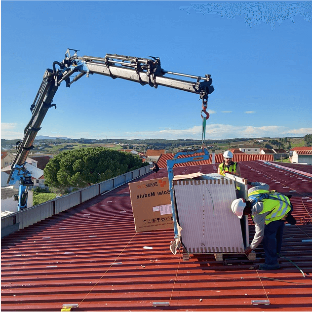 Workers installing solar panels on a roof with the help of a crane